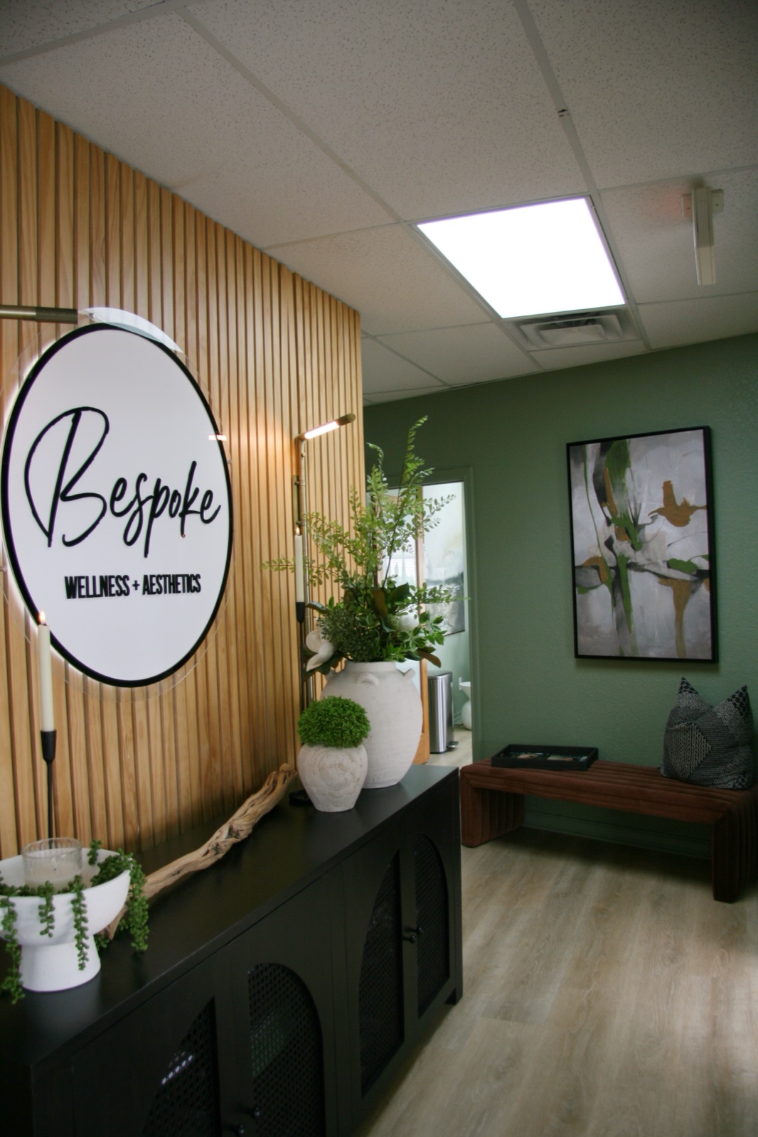 The Bespoke entryway — natural-wood slat wall with the Bespoke wellness & aesthetics logo, ferns, and the sage-toned waiting area beyond